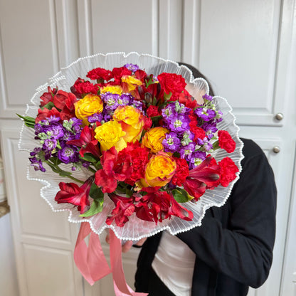 Vibrant red, yellow, and purple mixed flower bouquet with a white ruffled wrap.