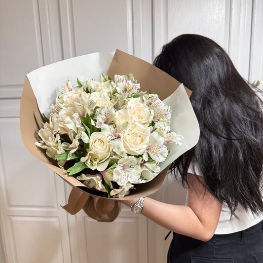 White roses and striped alstroemeria bouquet wrapped in brown paper, held by a person.