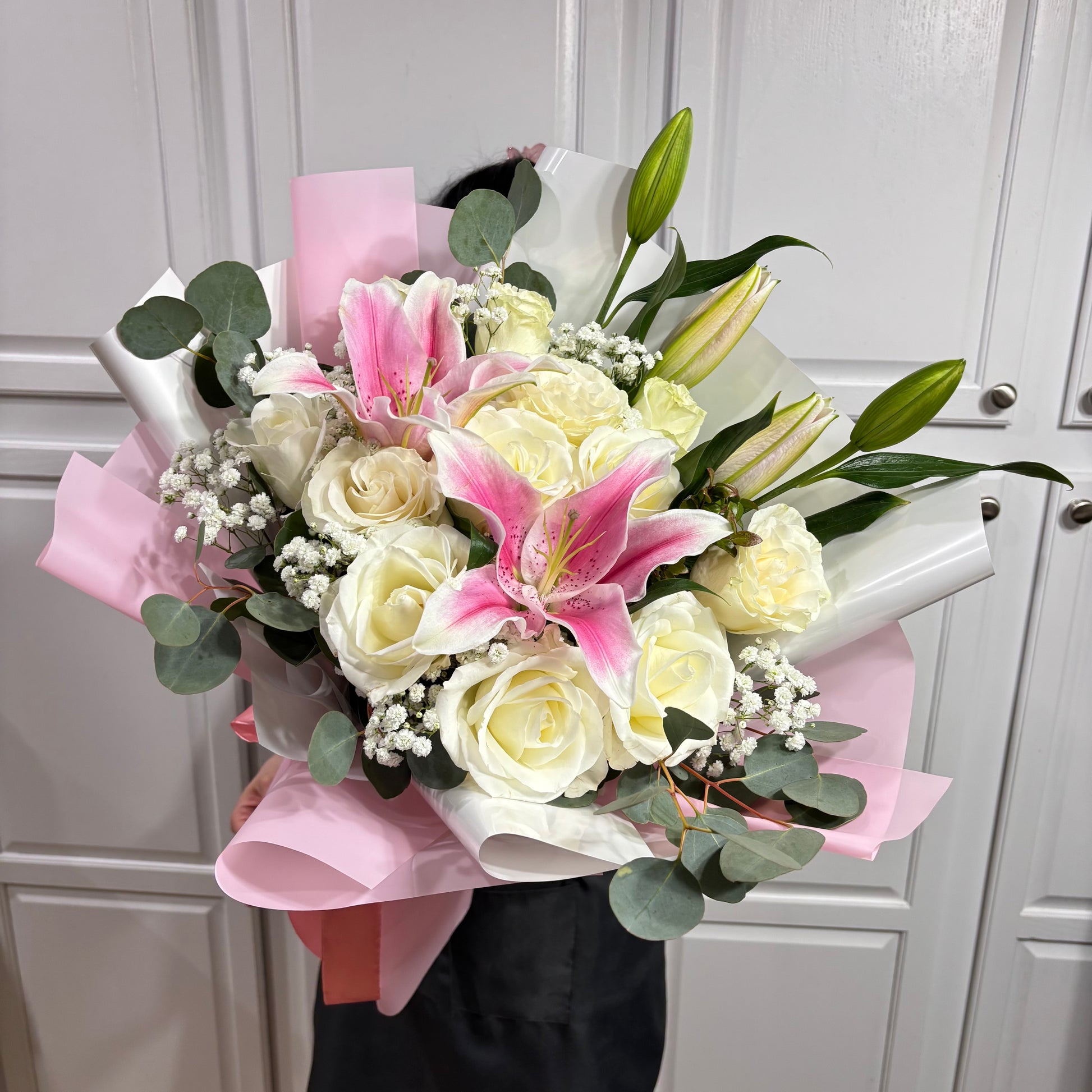 A beautiful bouquet of white roses, pink lilies, and eucalyptus wrapped in pink paper.