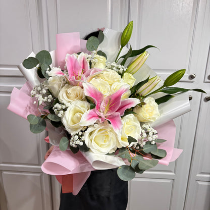 A beautiful bouquet of white roses, pink lilies, and eucalyptus wrapped in pink paper.
