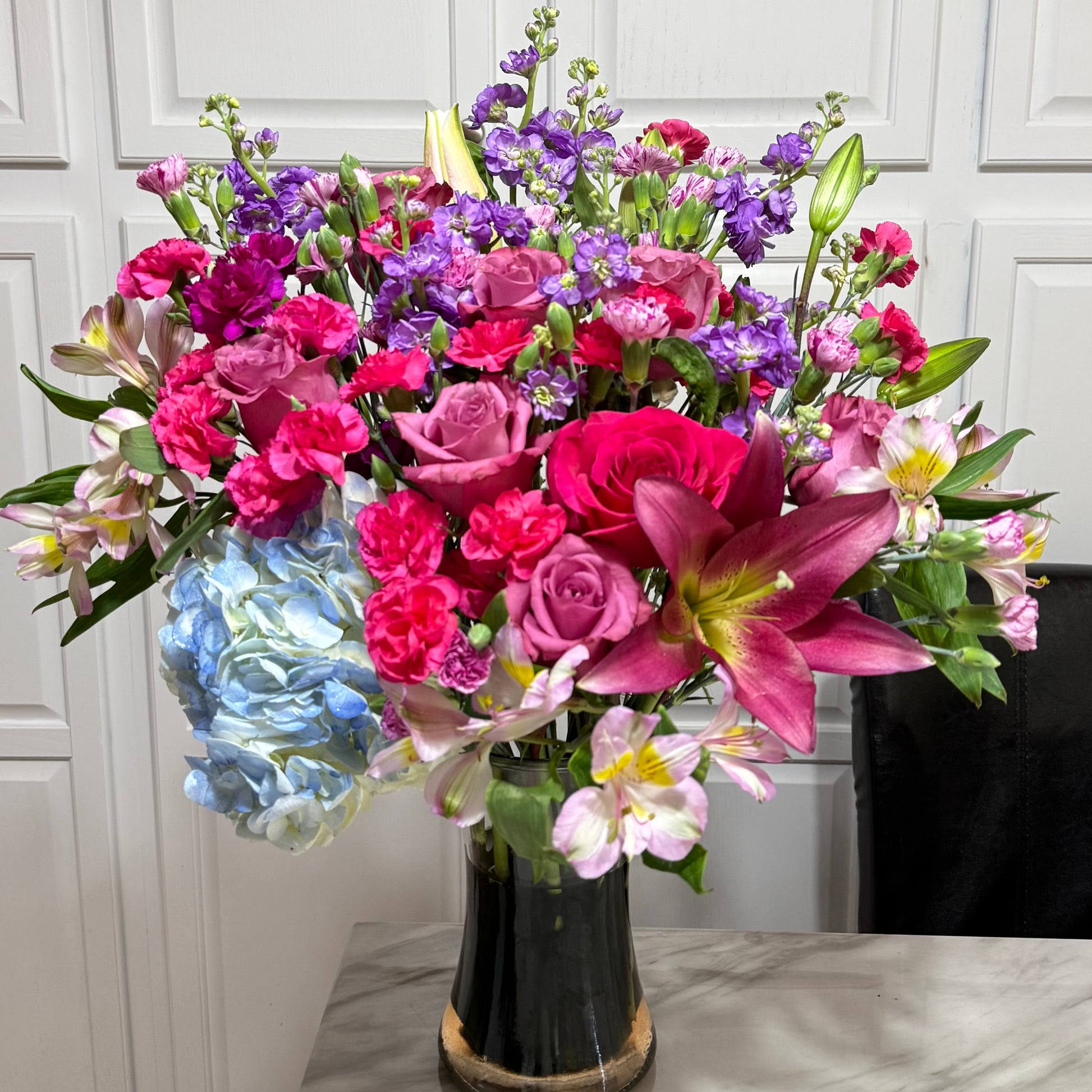 Large, colorful floral bouquet with pink roses, purple stock, and blue hydrangeas.