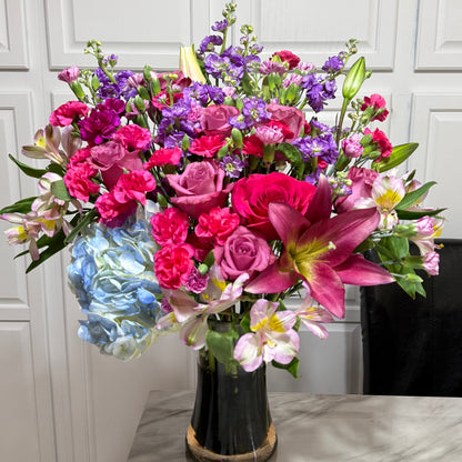 Large, colorful floral bouquet with pink roses, purple stock, and blue hydrangeas.