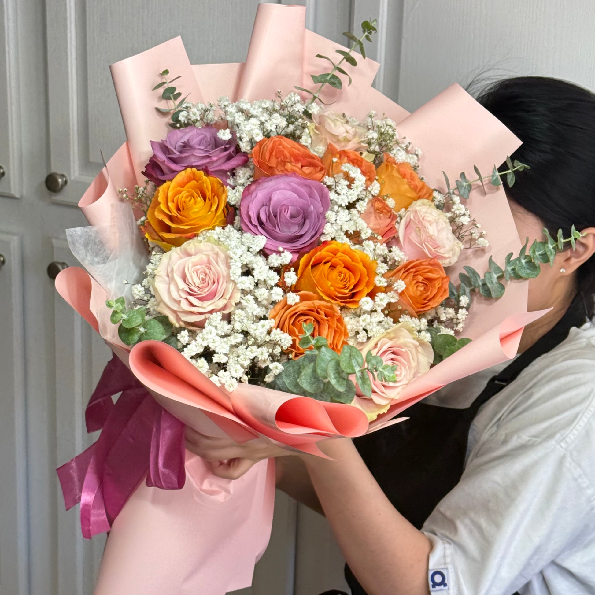 Large bouquet of colorful roses and baby's breath wrapped in pink paper.