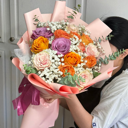 Large bouquet of colorful roses and baby's breath wrapped in pink paper.