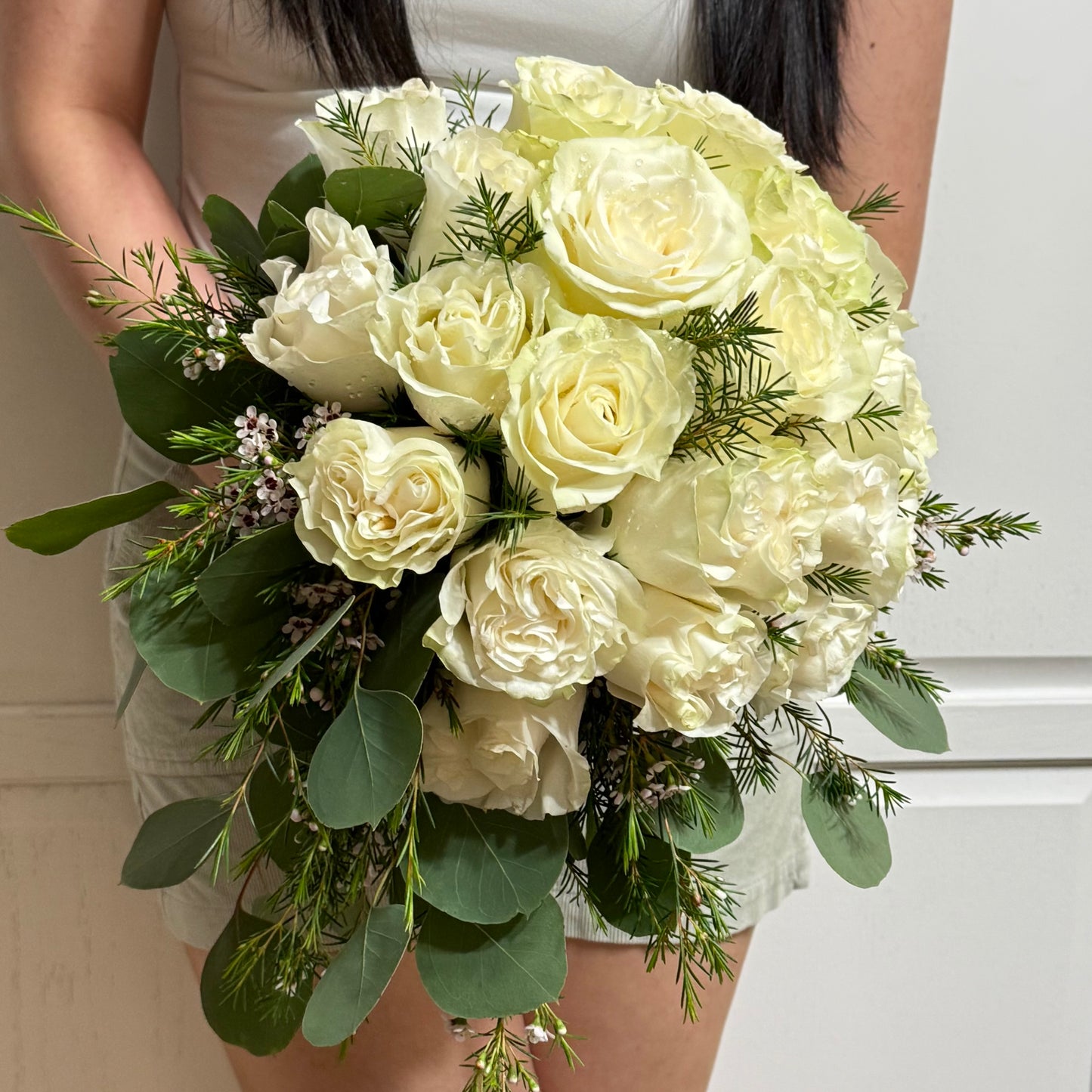 Cascading white rose bridal bouquet with green eucalyptus and small purple flowers.