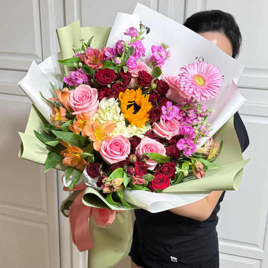 Vibrant bouquet with a yellow sunflower, pink roses, and mixed colorful blooms.