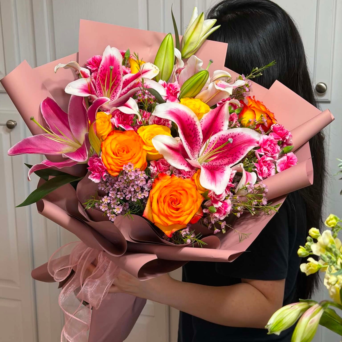 A vibrant bouquet of pink lilies and orange roses wrapped in pink paper.