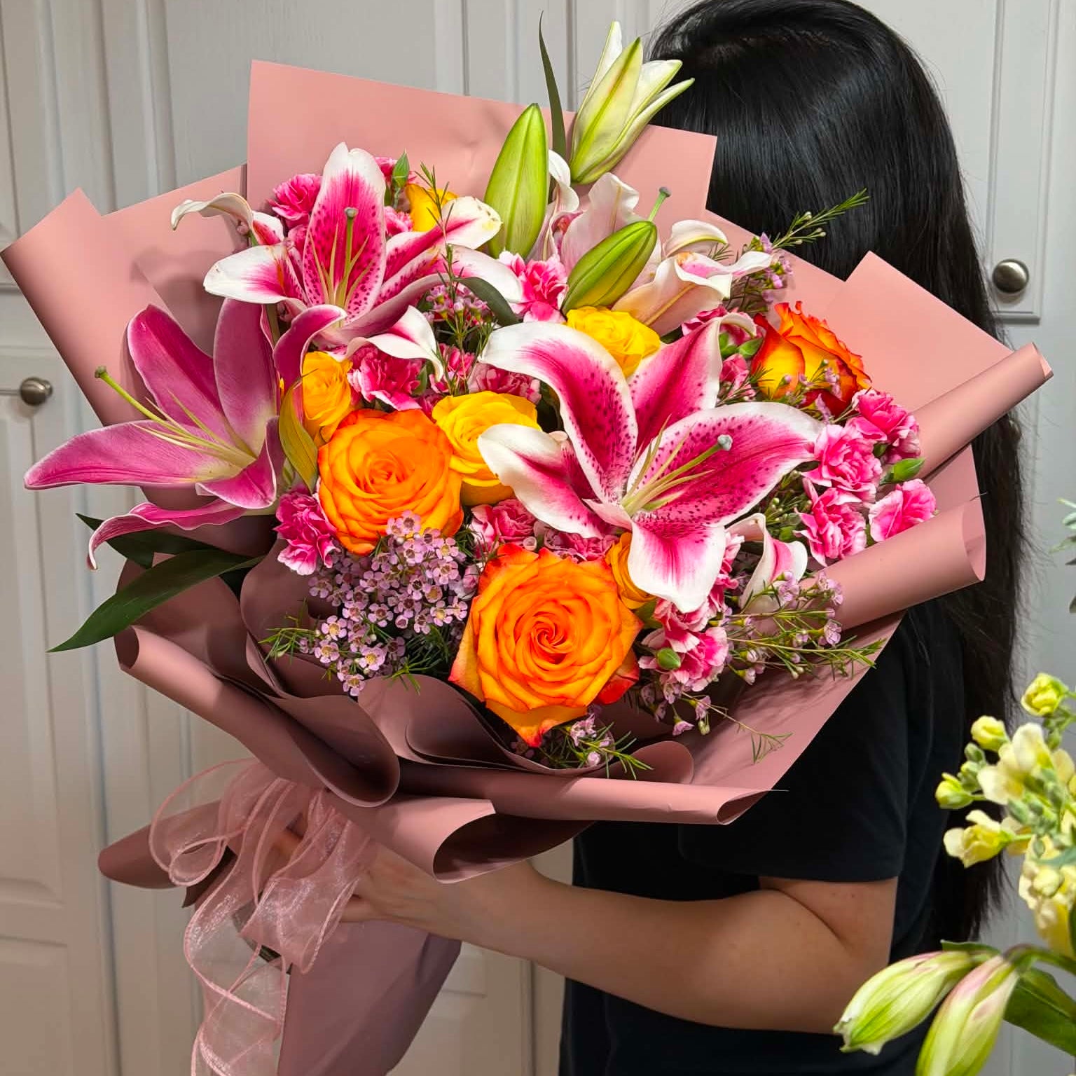 A vibrant bouquet of pink lilies and orange roses wrapped in pink paper.