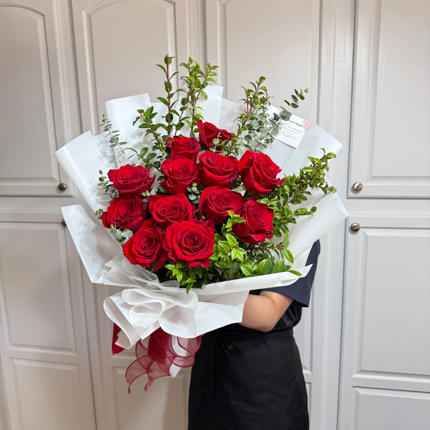Vibrant red rose bouquet with green foliage in white wrapping, held by a person.