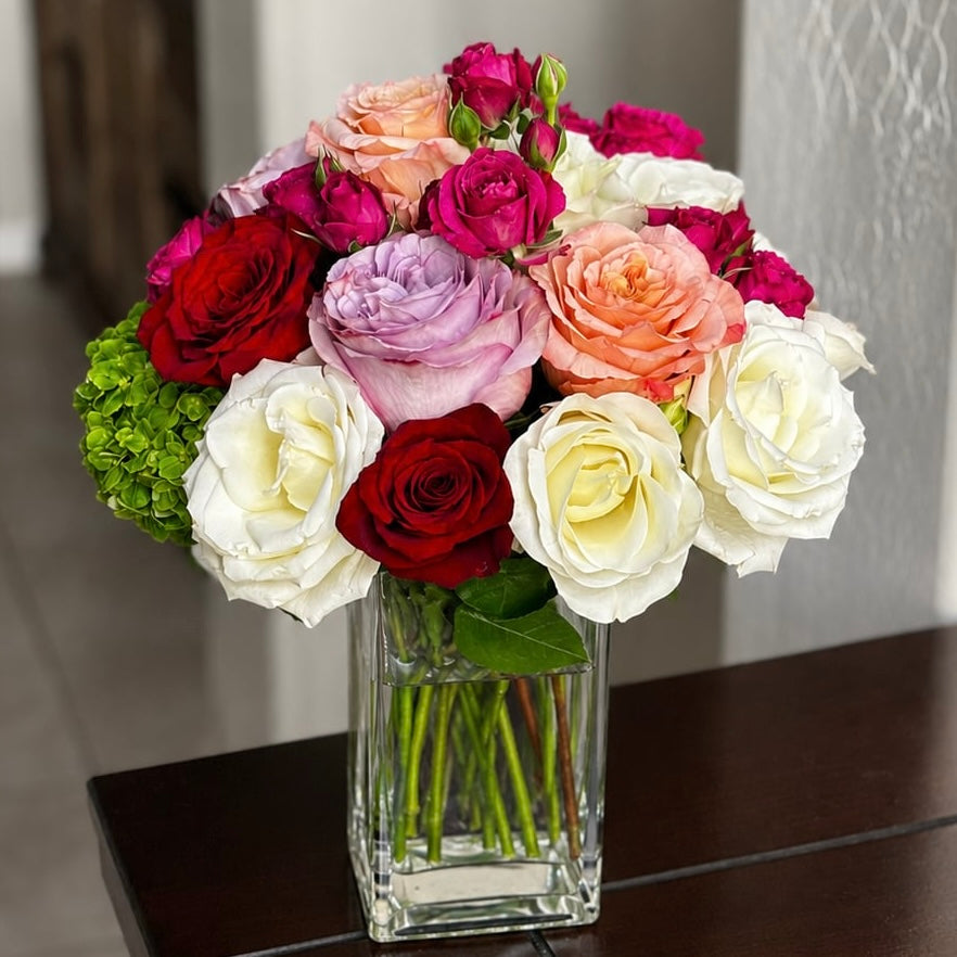 A vibrant bouquet of red, white, pink, and purple roses in a clear glass vase.