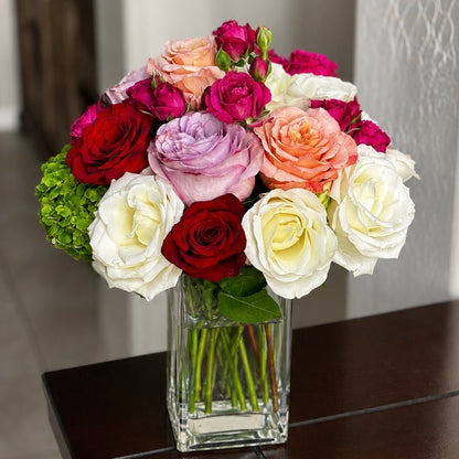 A vibrant bouquet of red, white, pink, and purple roses in a clear glass vase.