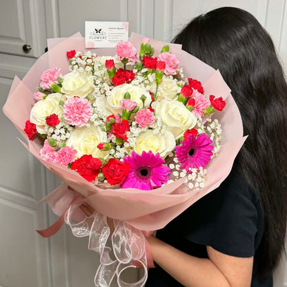Pink-wrapped bouquet with white roses, red and pink carnations, and fuchsia gerbera daisies.
