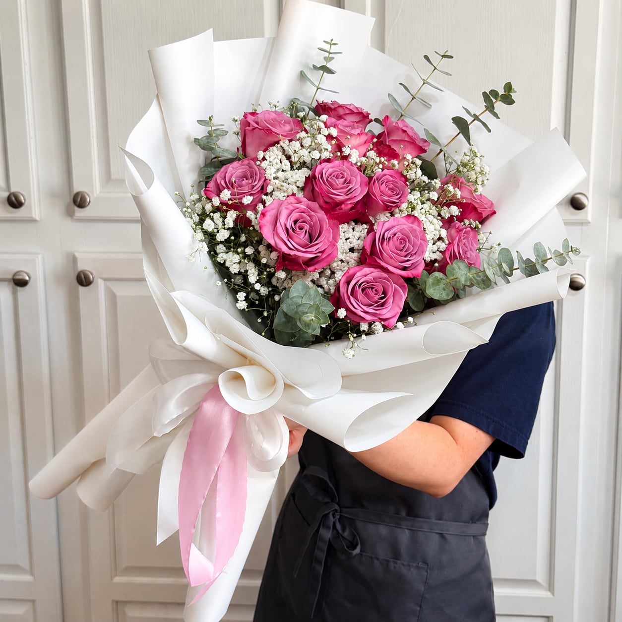 Vibrant pink rose bouquet with baby's breath and eucalyptus, wrapped in white with a pink ribbon.