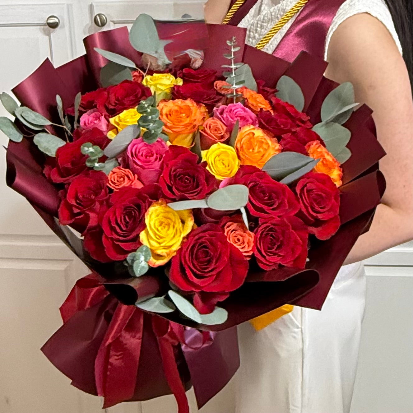 Vibrant bouquet of red, yellow, and orange roses wrapped in burgundy paper.