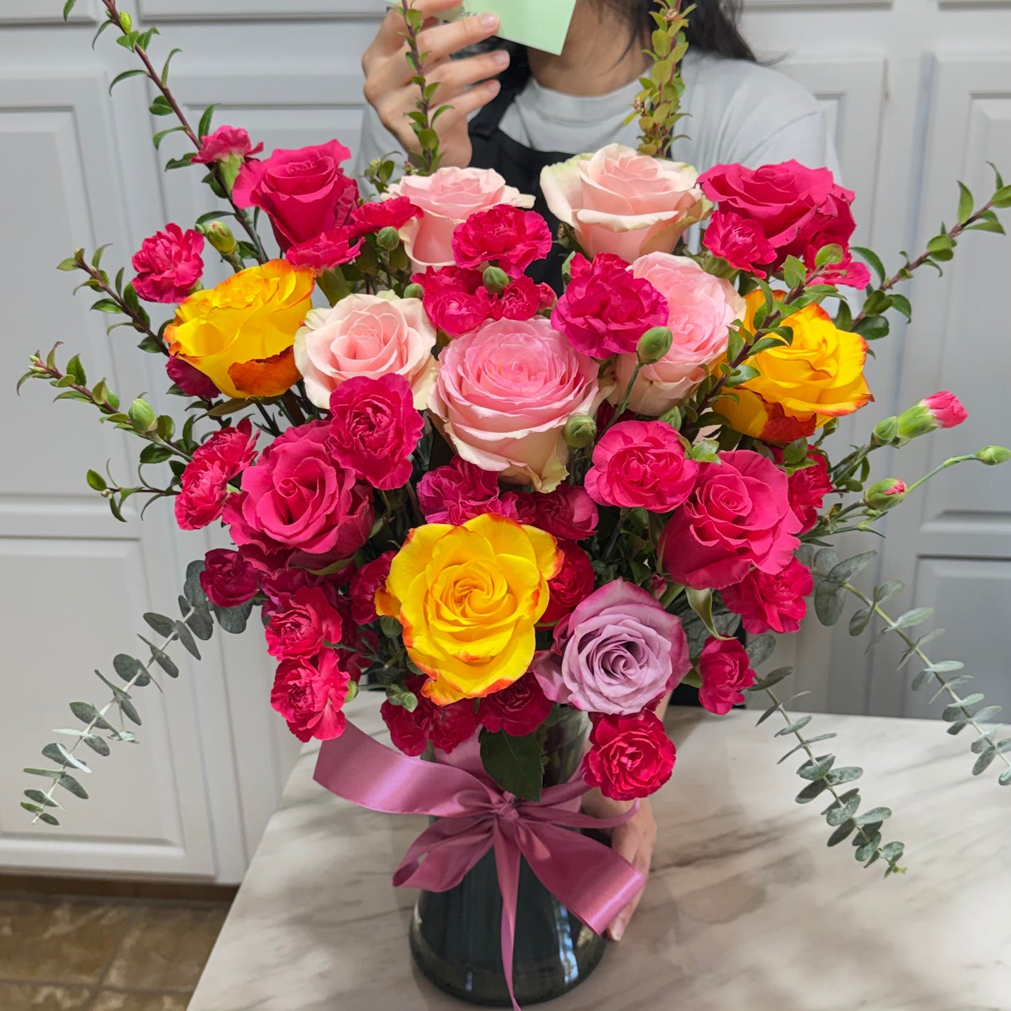 Vibrant bouquet of pink, yellow, and lavender roses and carnations in a vase.