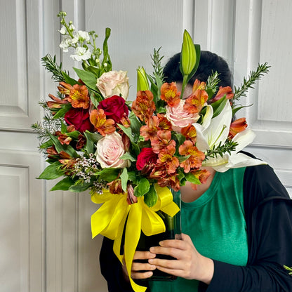Vibrant bouquet of red, pink, orange, and white flowers with a yellow ribbon.