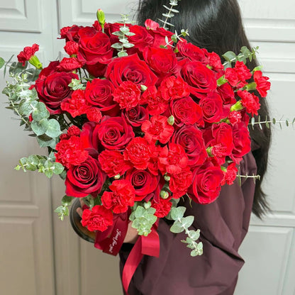 A person holds a large bouquet of vibrant red roses and carnations with eucalyptus.