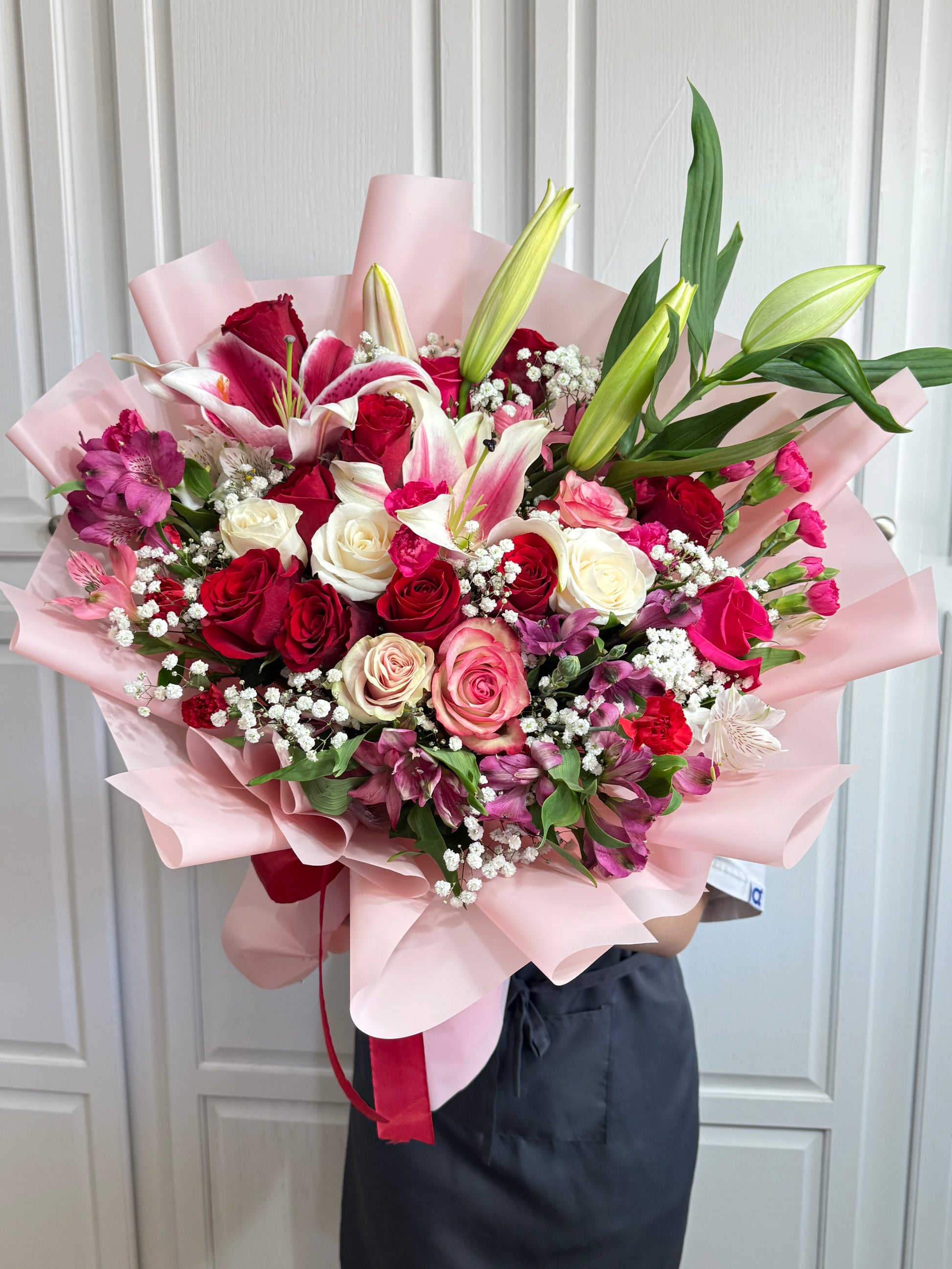 Large bouquet of red, white, and pink roses, lilies, and filler flowers wrapped in pink.