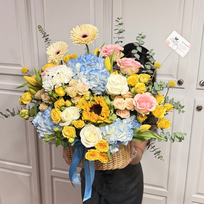 Large wicker basket filled with vibrant yellow, blue, and pink spring flowers.