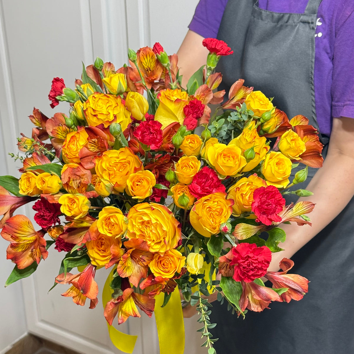 Bright bouquet of yellow and orange roses, red carnations, and alstroemeria.