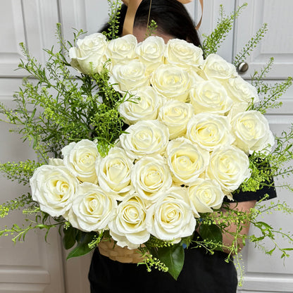A large, heart-shaped bouquet of white roses and green foliage in a woven basket.