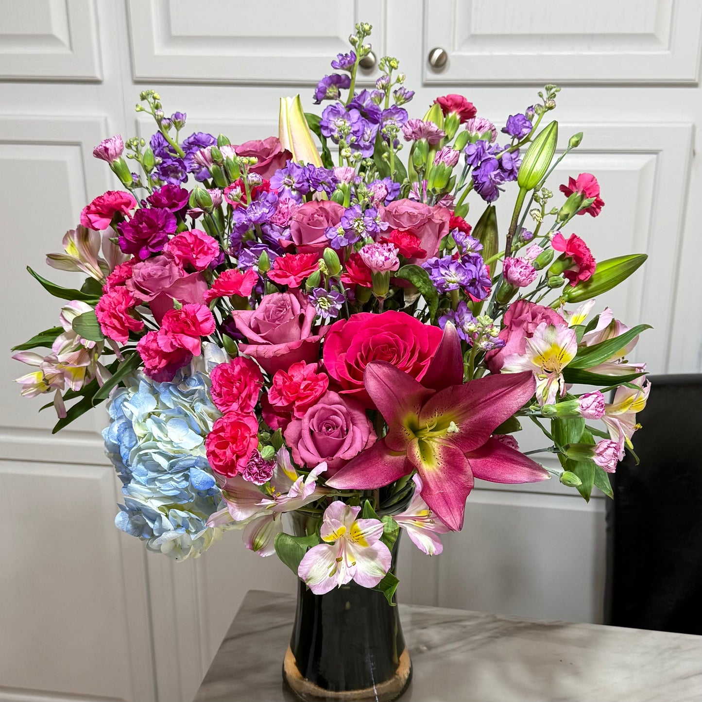 Lush bouquet of pink roses, purple snapdragons, blue hydrangeas, and fuchsia lilies.