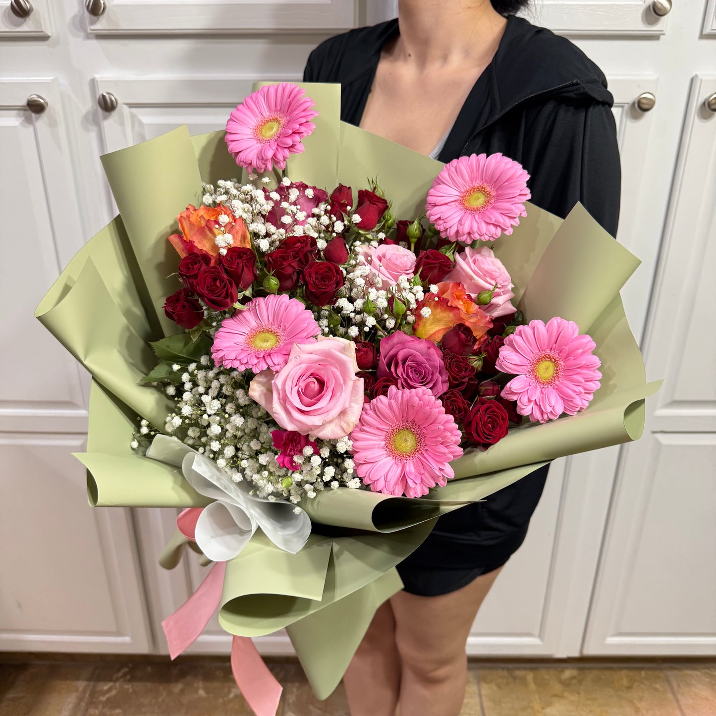 Vibrant bouquet of pink gerberas, red, and orange roses in green wrap.