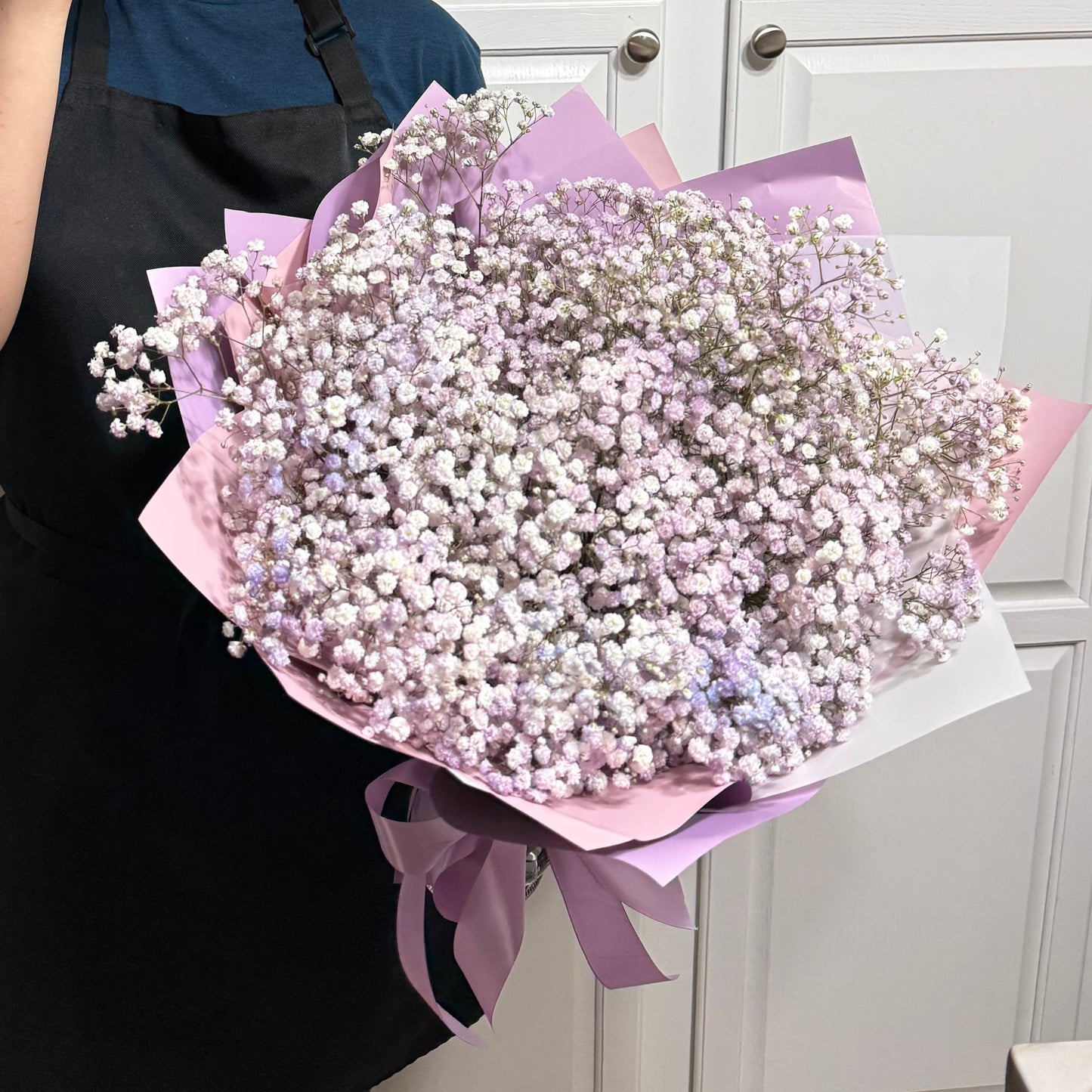 Large bouquet of delicate purple and white baby's breath flowers in pastel wrapping.