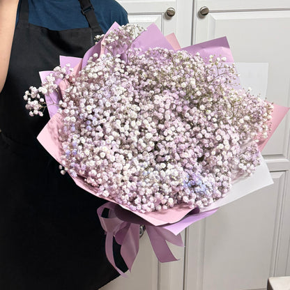 Large bouquet of delicate purple and white baby's breath flowers in pastel wrapping.