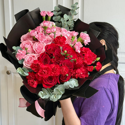 Vibrant red and pink roses and carnations bouquet wrapped in black paper.