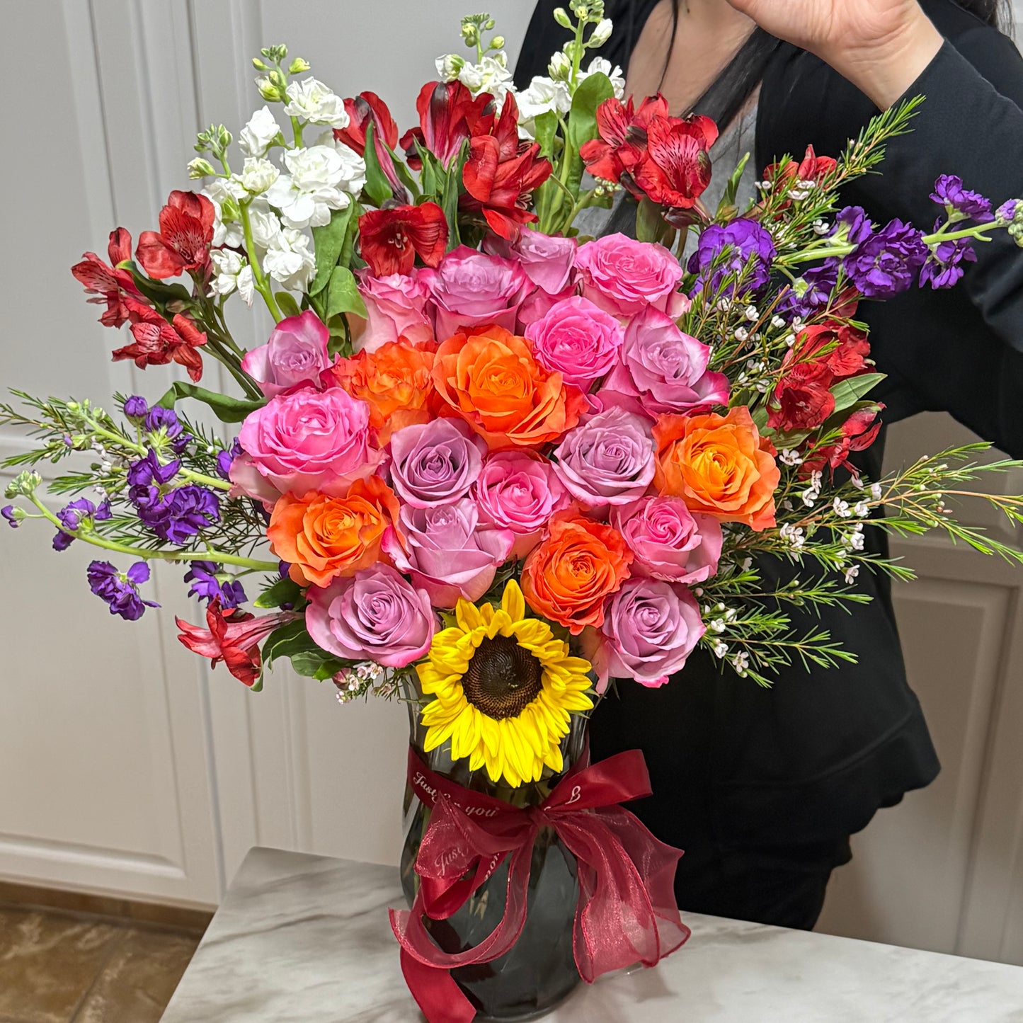 Colorful bouquet with roses, stock, alstroemeria, and a sunflower in a glass vase.