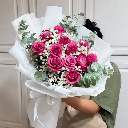 A vibrant bouquet of pink roses, white baby's breath, and eucalyptus, wrapped in white.