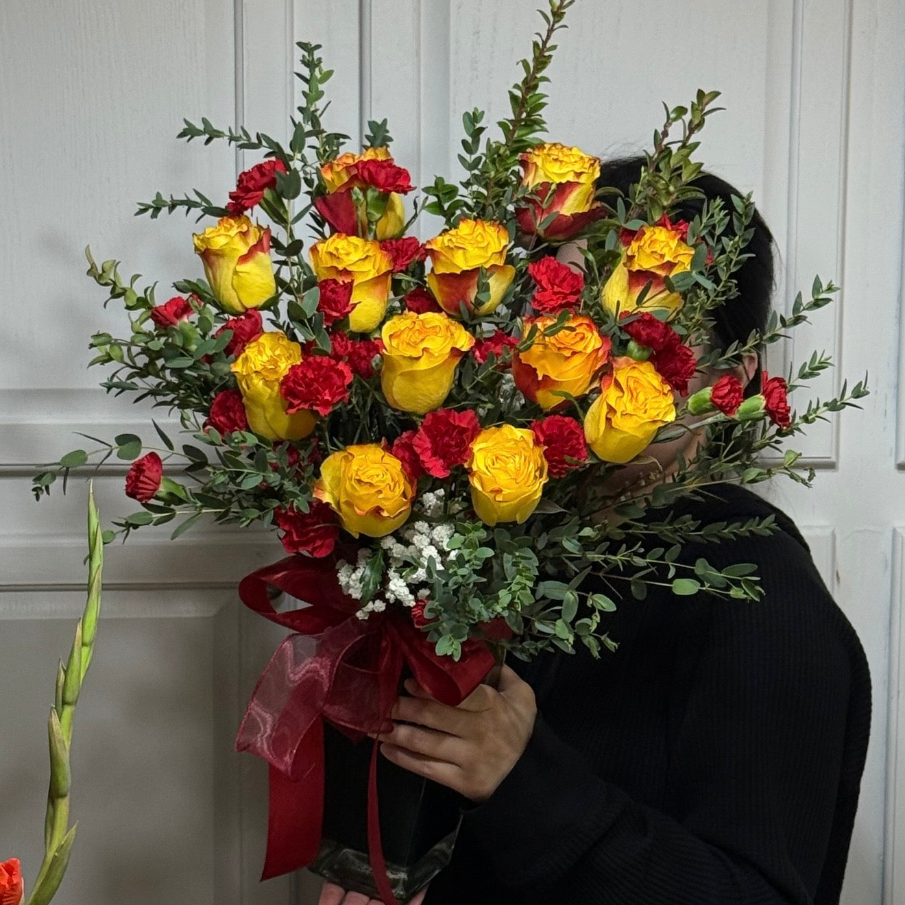 Vibrant yellow roses and red carnations bouquet with green leaves and red ribbon.