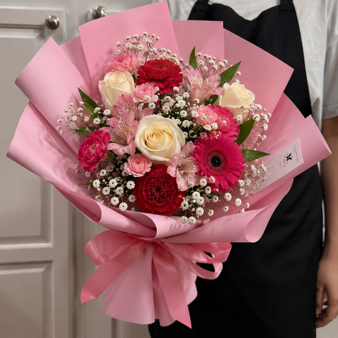 A vibrant pink-wrapped bouquet featuring white roses, red carnations, and baby's breath.