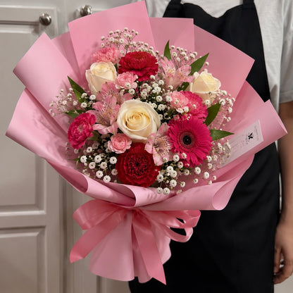 A vibrant pink-wrapped bouquet featuring white roses, red carnations, and baby's breath.