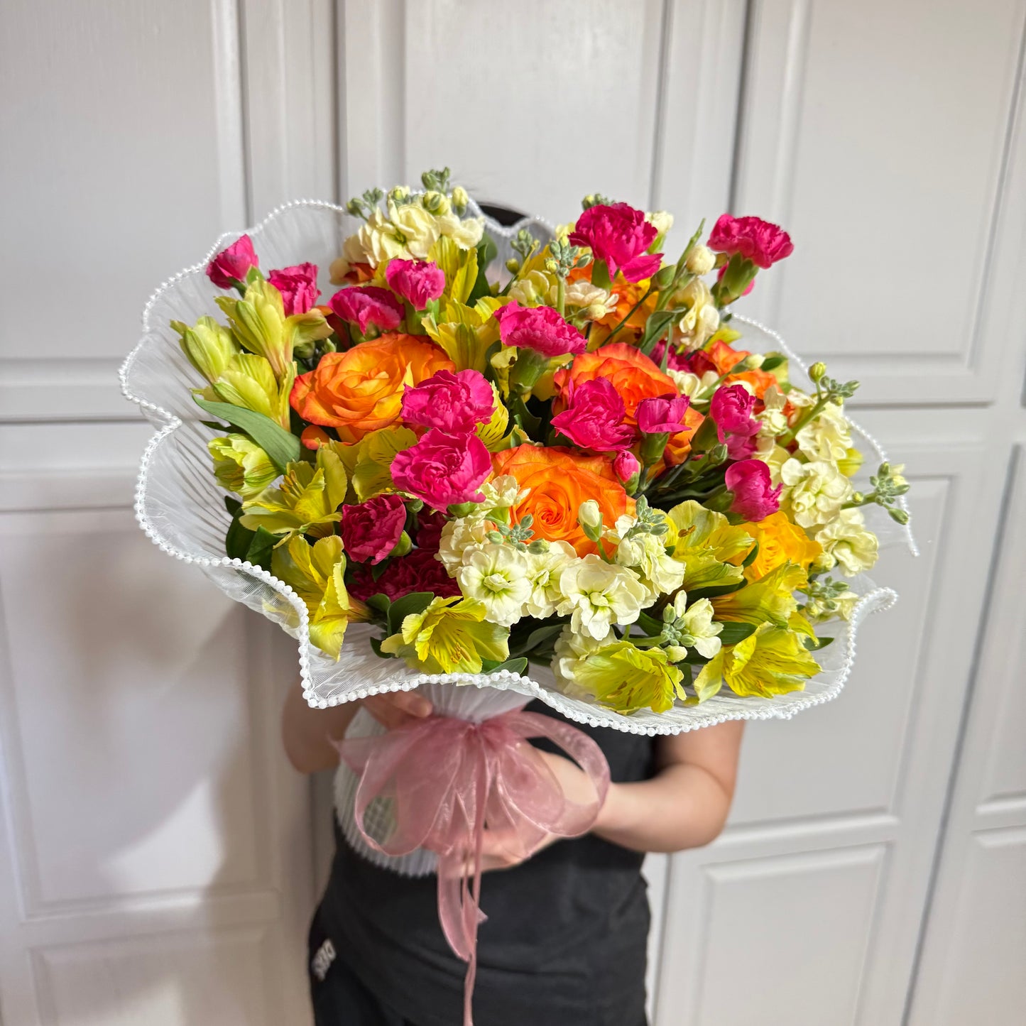 Vibrant mixed flower bouquet with orange, pink, and yellow flowers in white wrap.