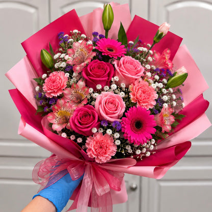 A vibrant bouquet of pink and fuchsia flowers wrapped in pink paper.