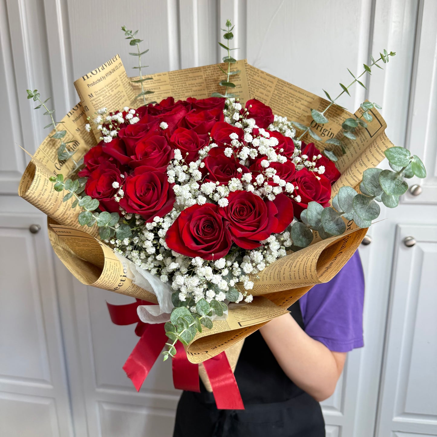 Classic red rose bouquet with white baby's breath, wrapped in vintage newspaper print.