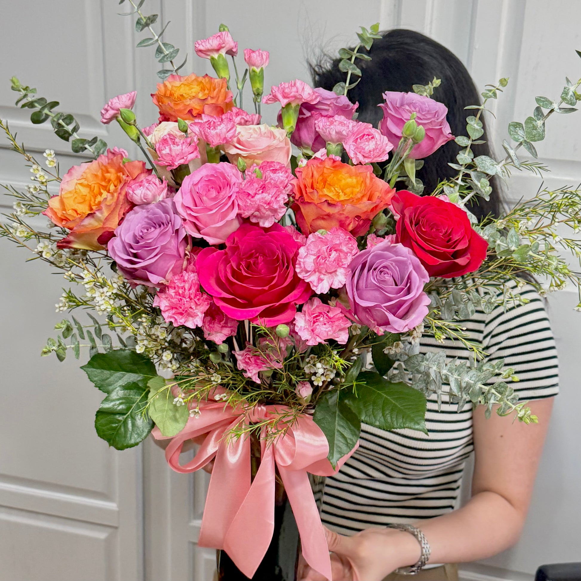 Vibrant bouquet of pink, purple, orange, and red roses with a pink ribbon.