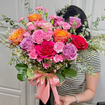 Vibrant bouquet of pink, purple, orange, and red roses with a pink ribbon.