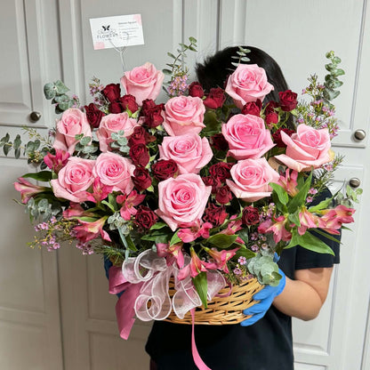 Woven basket overflowing with vibrant pink and red roses and greenery.