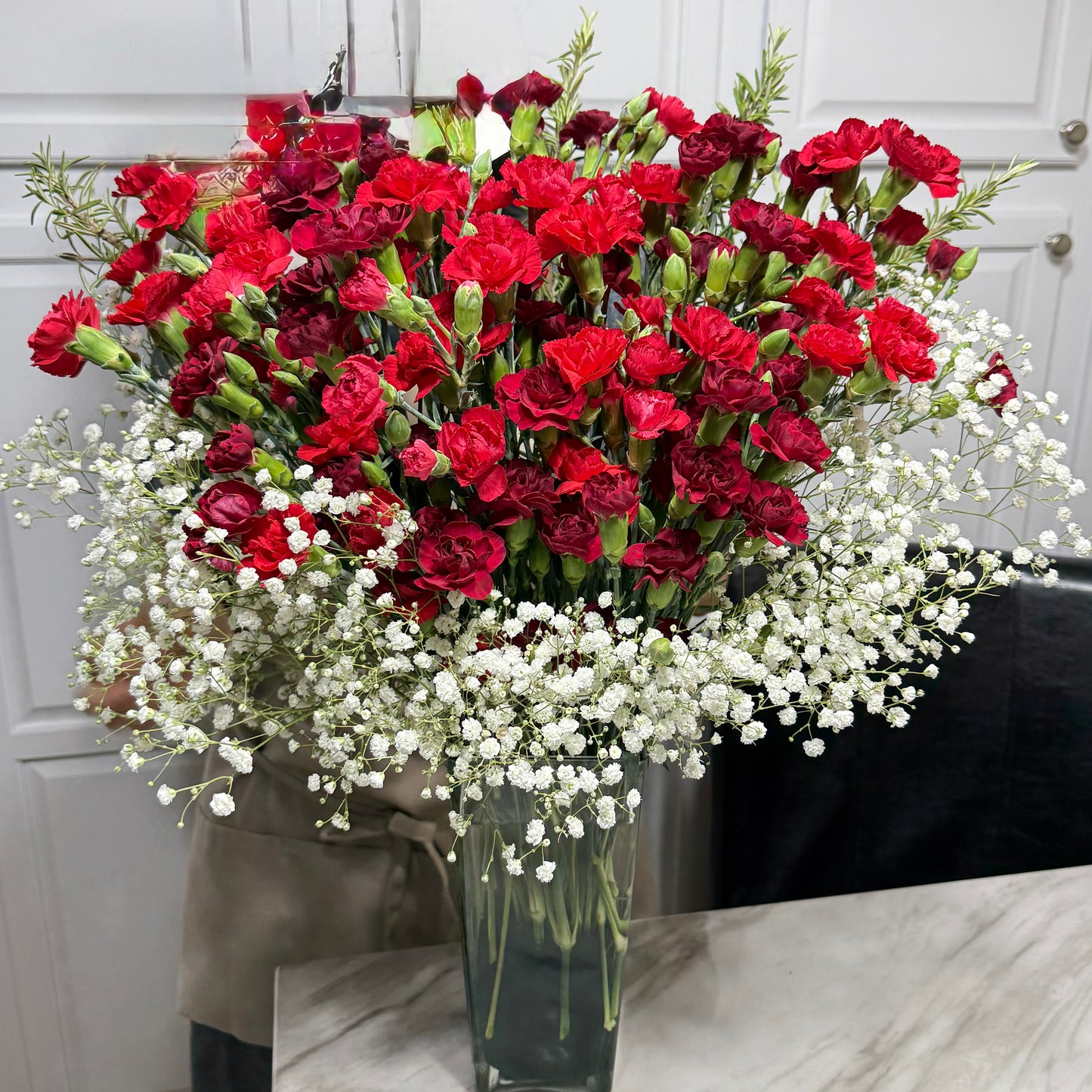 A vibrant bouquet of red carnations and white baby's breath in a clear vase.
