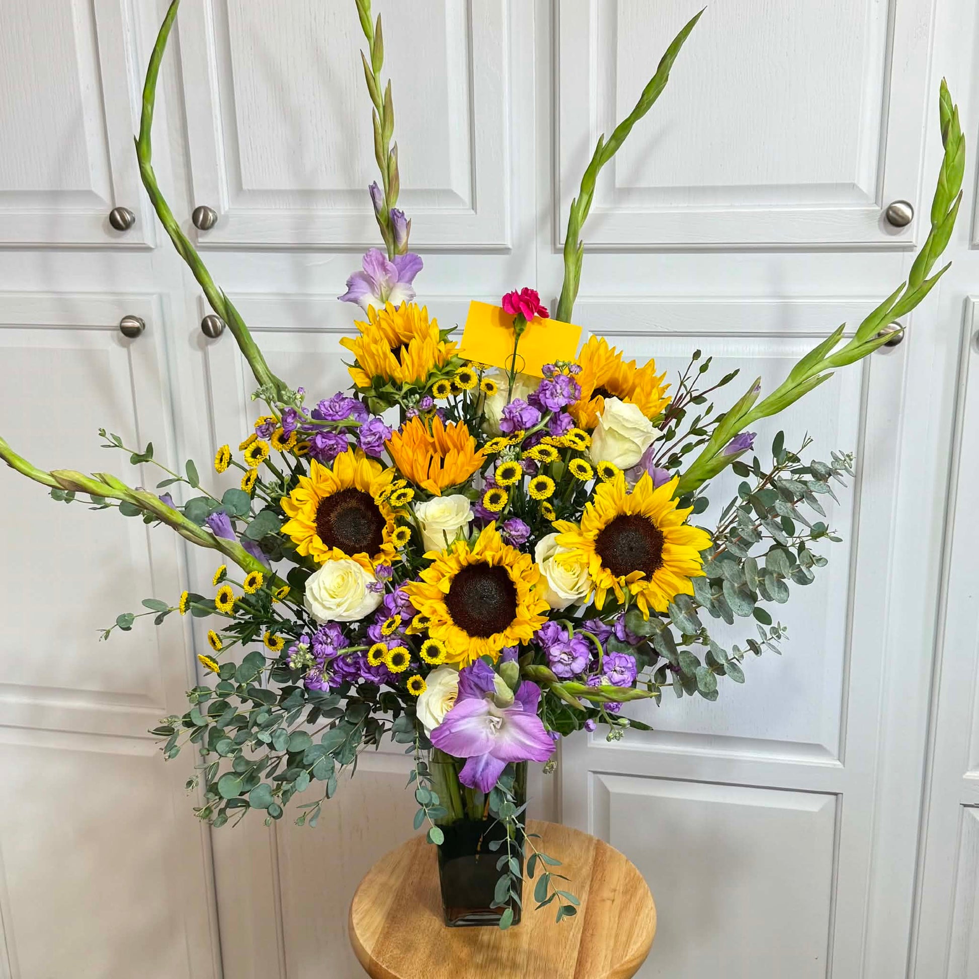 Stunning bouquet of yellow sunflowers, white roses, and purple gladiolus in a vase.