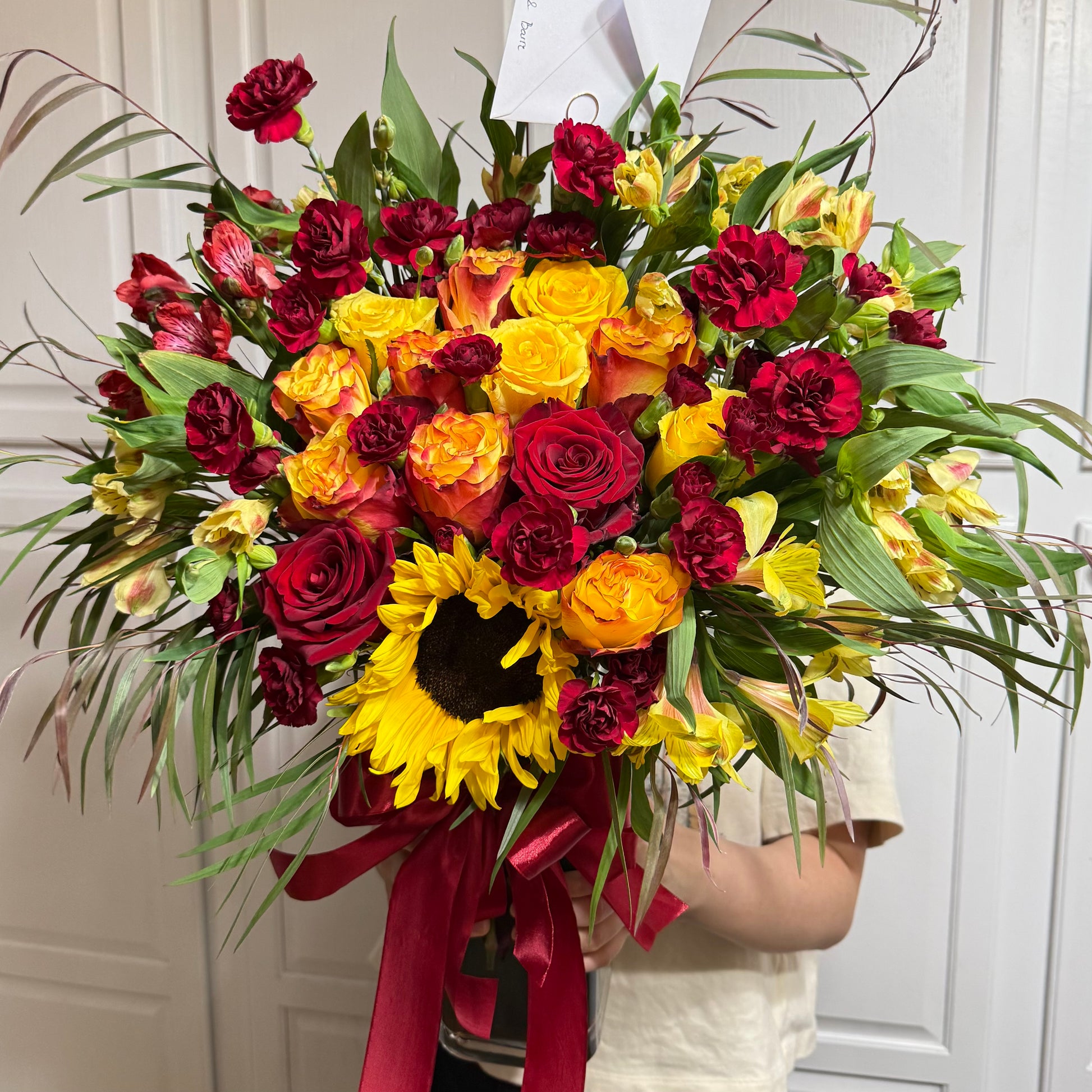 Vibrant red and yellow flower bouquet featuring roses, carnations, and a sunflower.