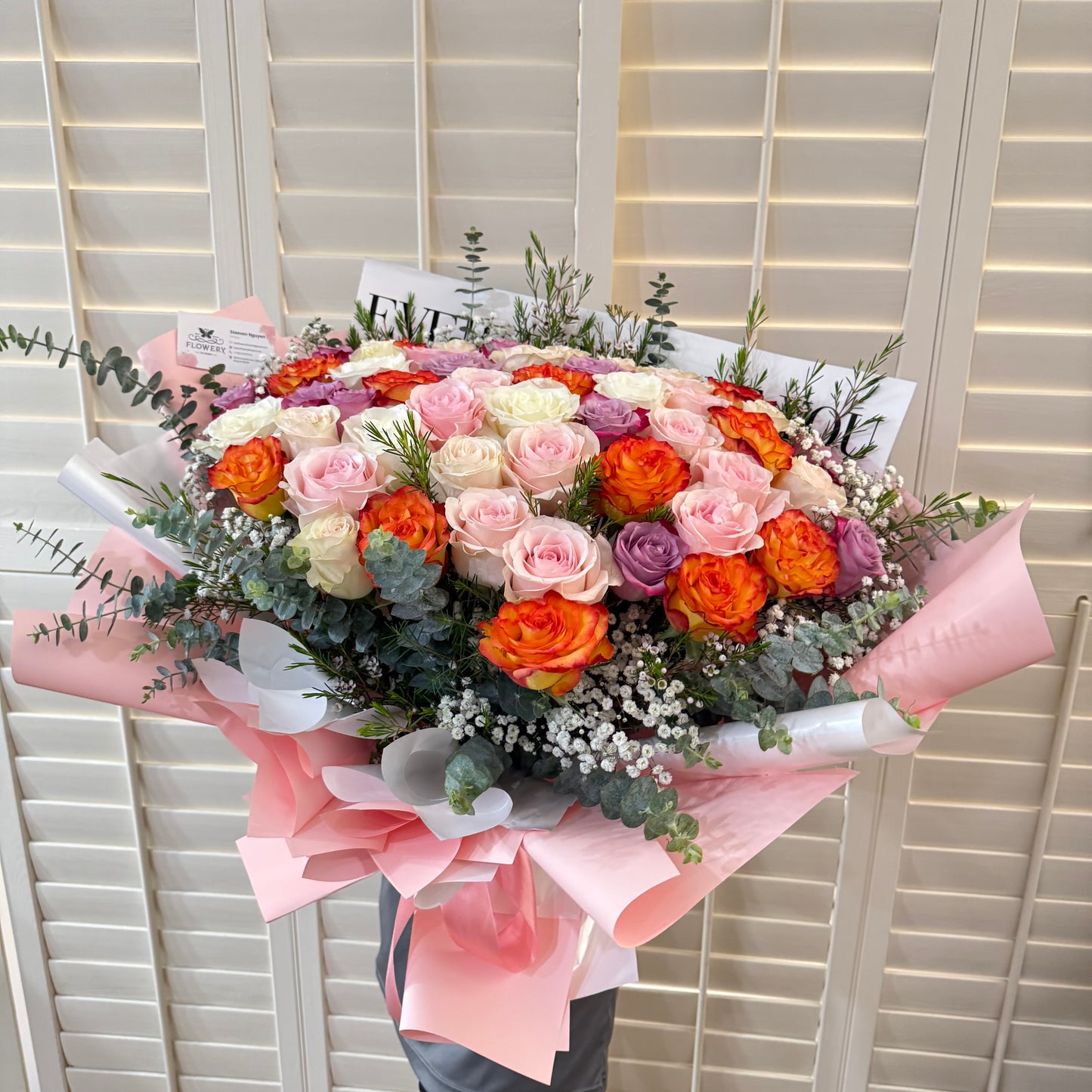 Large bouquet of colorful roses wrapped in pink paper.