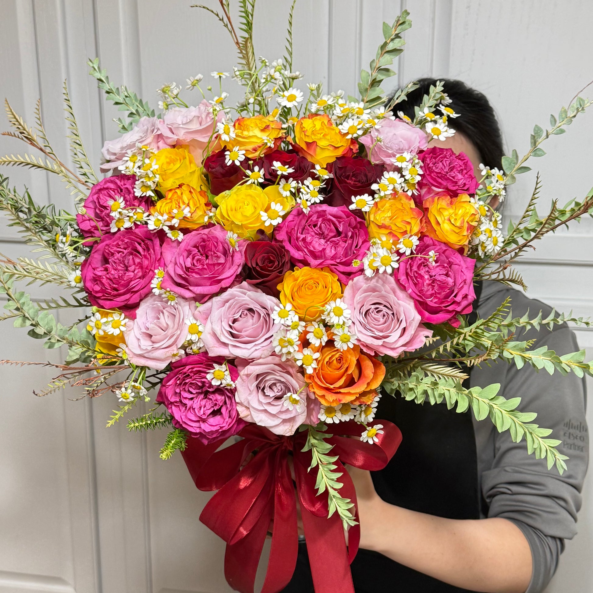 Large bouquet of vibrant pink, yellow, orange, and red roses with daisies.