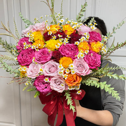 Large bouquet of vibrant pink, yellow, orange, and red roses with daisies.