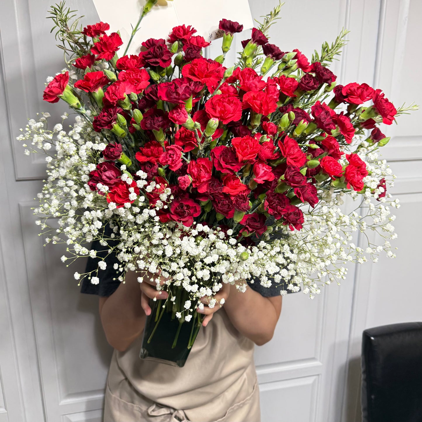 Vibrant red and dark red carnations with delicate white baby's breath in a clear vase.