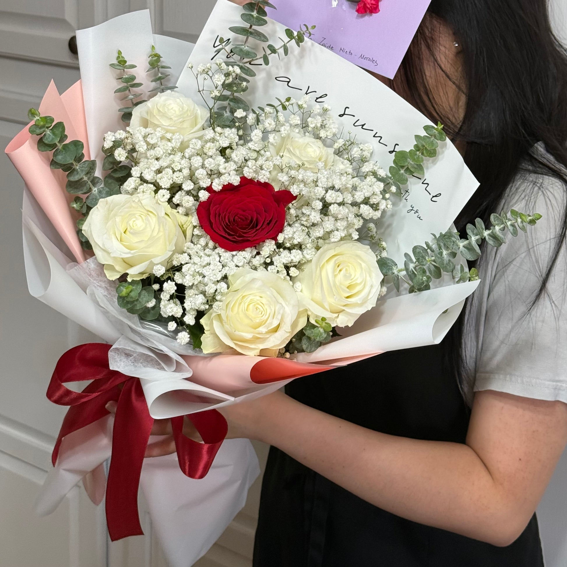 Person holding a bouquet of white and red roses, baby's breath, and eucalyptus.