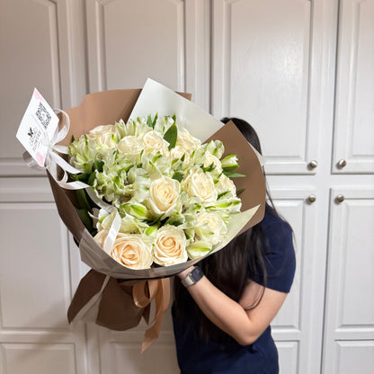 Large bouquet of cream roses and green filler flowers in brown and white wrap.